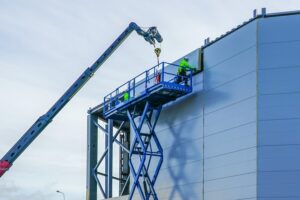 mężczyźni na podnośniku nożycowym mocujący element elewacji